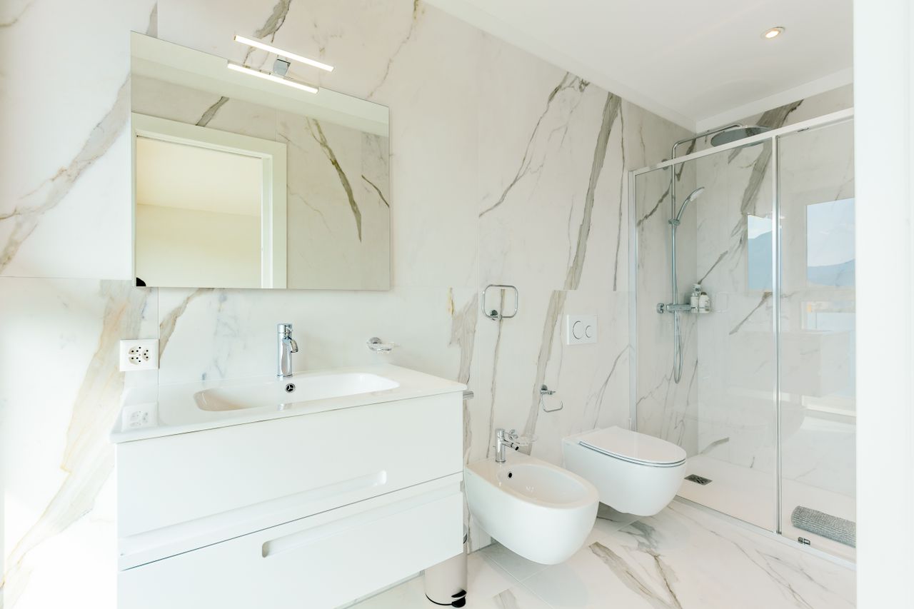 Elegant white bathroom featuring marble tiles and modern fixtures, perfect for a luxury home setting.